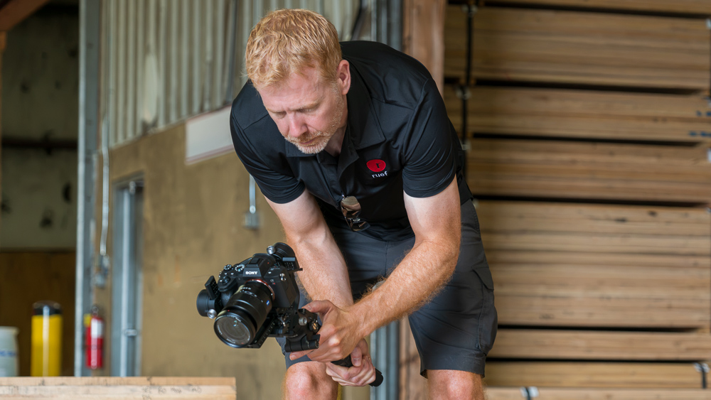 ruef Creative camera operator in a black shirt using a Sony Alpha camera on a gimbal to film hardwood lumber with tall stacks of hardwood lumber in the background.